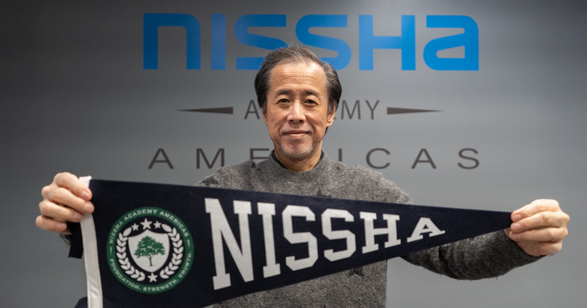 Nissha Chairman of the Board and Group CEO Junya Suzuki holding a pennant flag that says Nissha