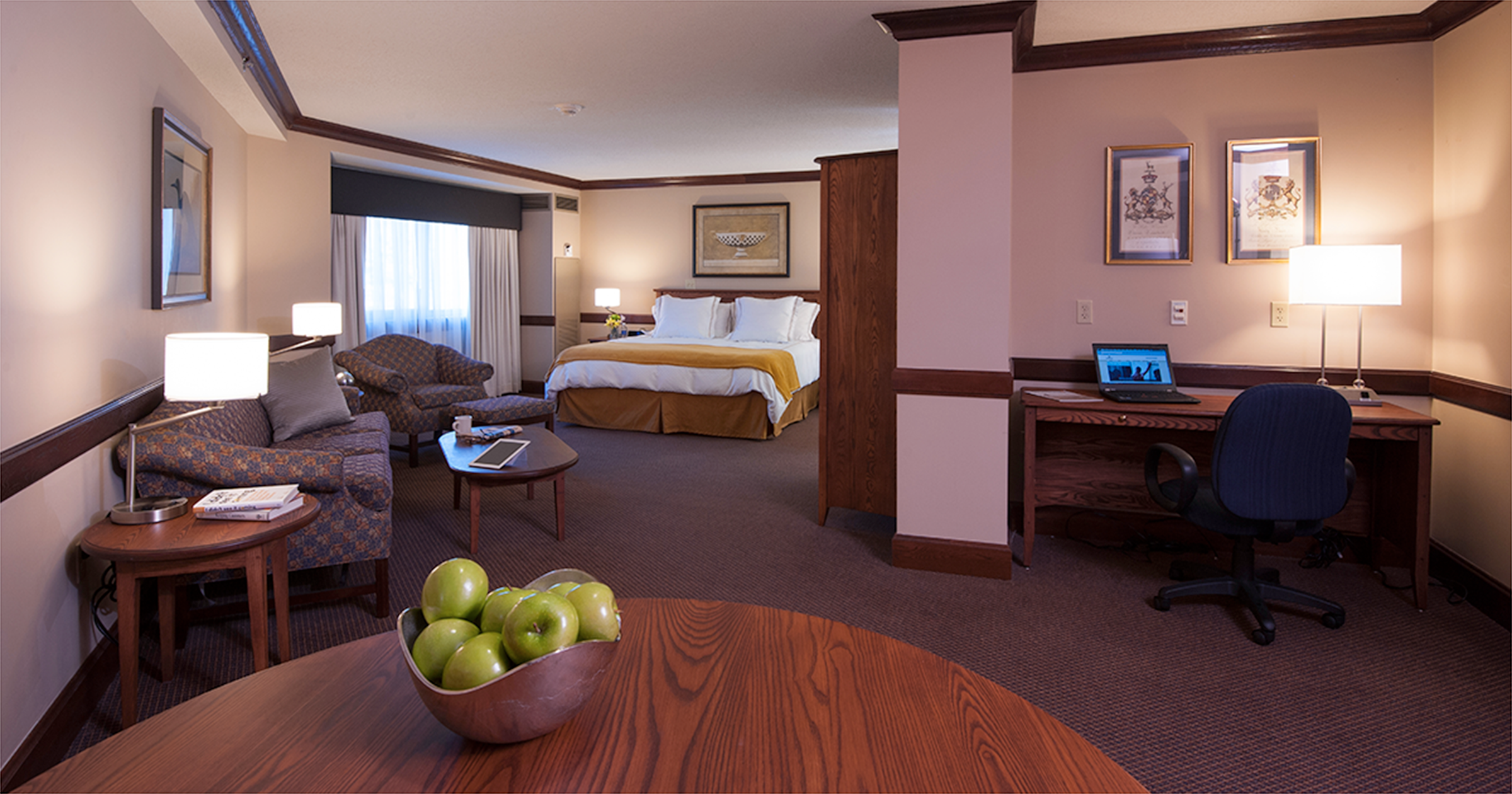 a view of a hotel bed with a bowl of green apples in near sight and a laptop in the corner.