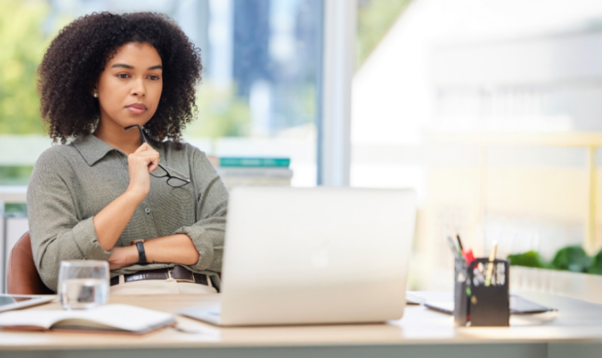 Woman holding glasses sitting and looking at a laptop
