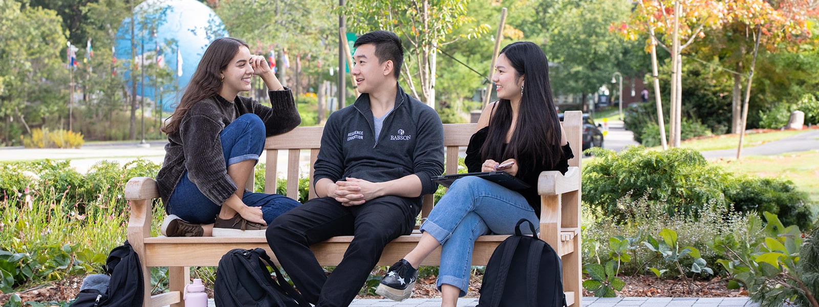 Three students sitting on a bench in front of a globe